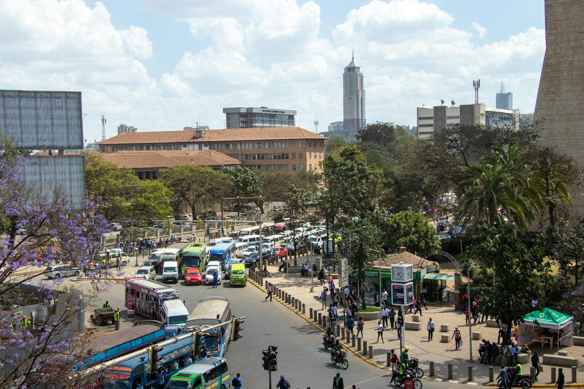 Pedestrians and vehicles move along a busy street in central Nairobi, Kenya, surrounded by commercial buildings and bustling urban activity.