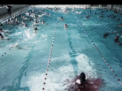 Dozens of swimmers fill the lanes of a crowded indoor swimming pool while it also fills up with a red substance.