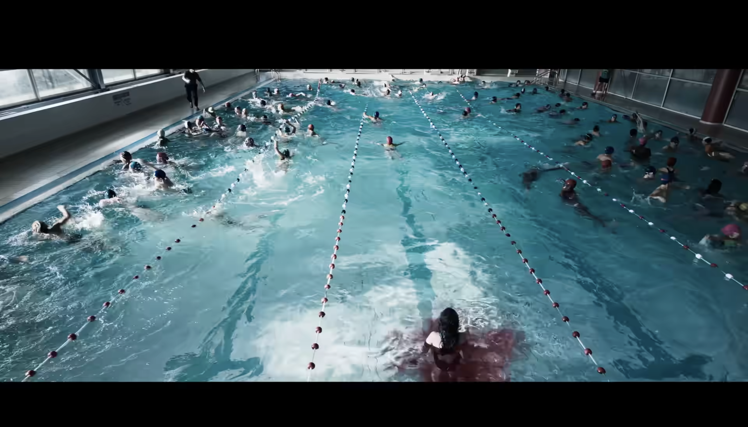Dozens of swimmers fill the lanes of a crowded indoor swimming pool while it also fills up with a red substance.