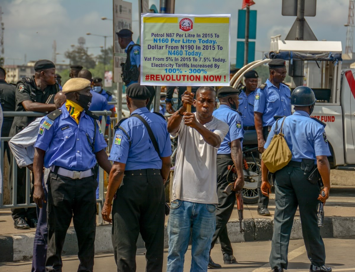 Man holding sign deriding fuel prices in front of police.