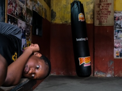 A teenager lies down in front of a punching bag in a boxing gym.