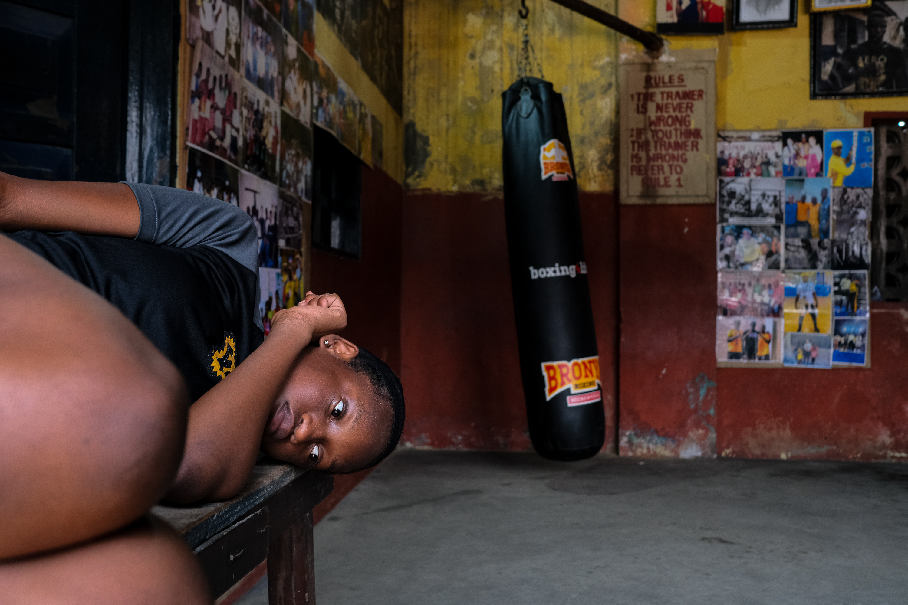A teenager lies down in front of a punching bag in a boxing gym.