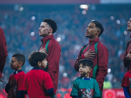 Moroccan footballers stand with their hands over their hearts during the national anthem before a match against Paraguay, accompanied by child mascots on the pitch.