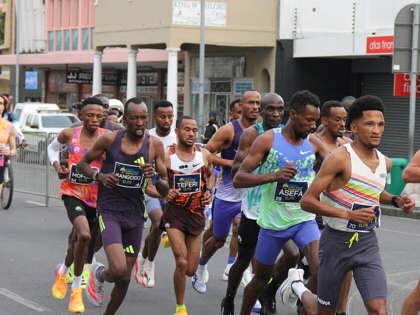 A pack of elite marathon runners races through a Cape Town city street during the 2026 Cape Town Marathon, accompanied by motorcycle escorts.