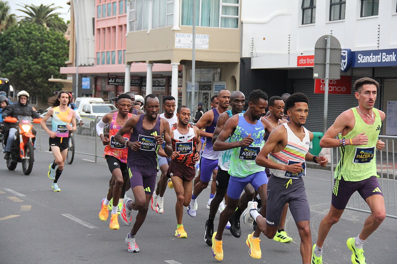 A pack of elite marathon runners races through a Cape Town city street during the 2026 Cape Town Marathon, accompanied by motorcycle escorts.