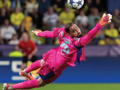 A goalkeeper clad in bright pink sports attire extends outward attempting to parry a football.
