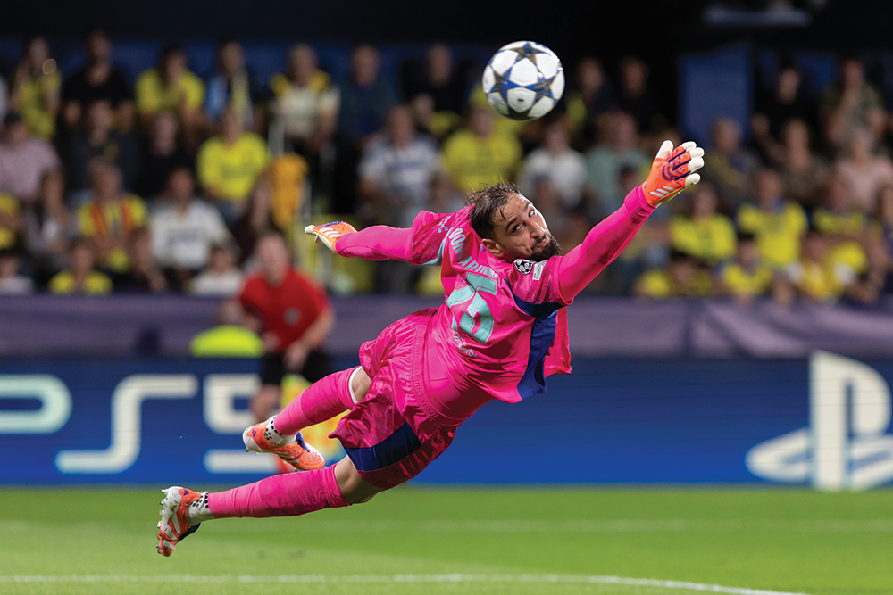 A goalkeeper clad in bright pink sports attire extends outward attempting to parry a football.