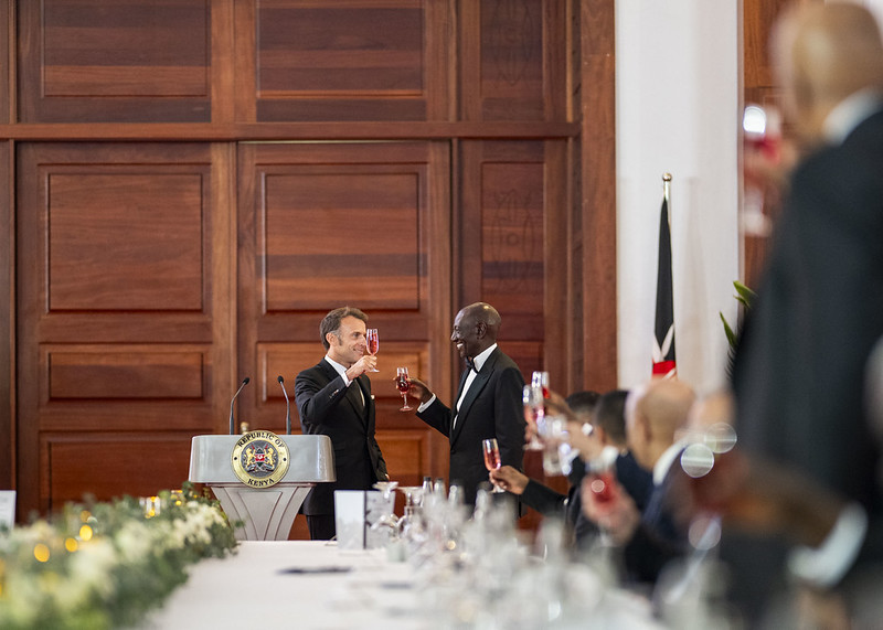 President William Ruto of Kenya and President Emmanuel Macron of France participate in a toast in a fancy ballroom.