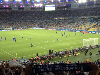 Players warming up on a football pitch in a packed stadium at nighttime.