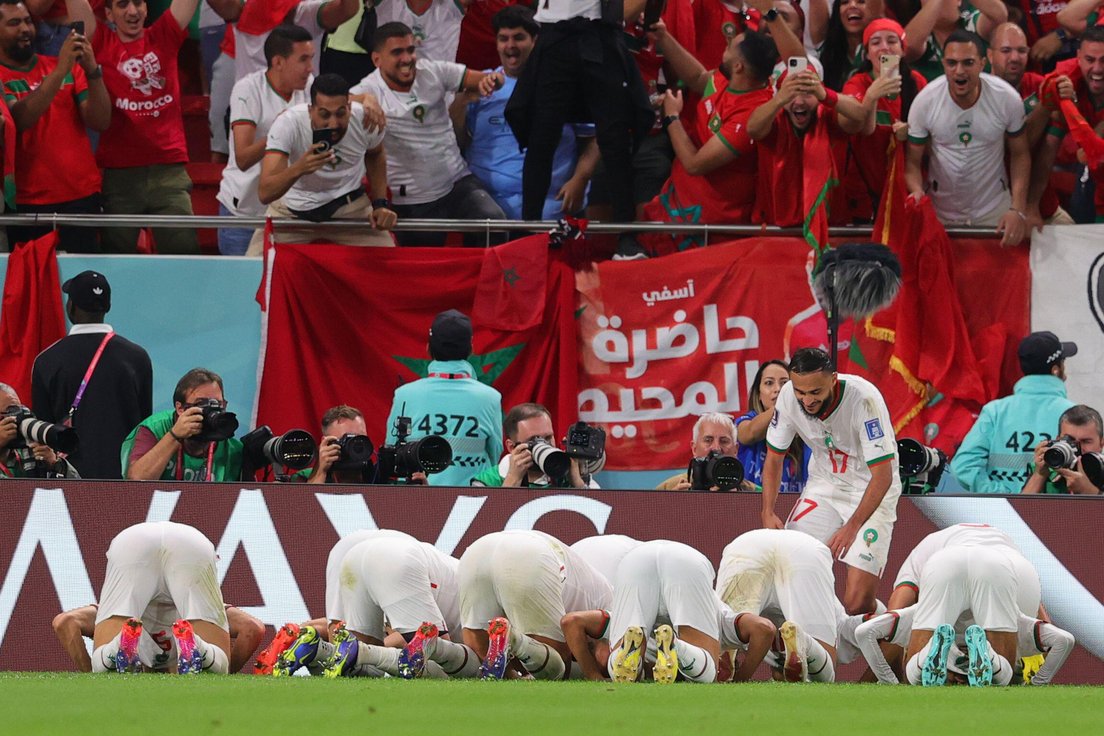 A group of football players dressed in white kneeling on the ground in a football stadium.