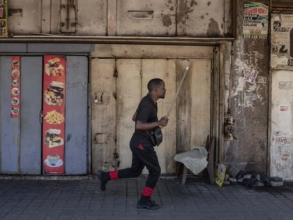 A man dressed in black runs past closed shops and weathered storefronts on a largely empty Johannesburg street.
