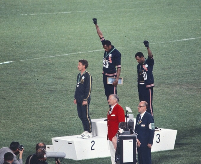 Olympic medallists Tommie Smith, Peter Norman, and John Carlos stand on the podium after the 200 metres at the 1968 Mexico City Olympics. Smith and Carlos bow their heads and raise black-gloved fists in protest against racial discrimination.
