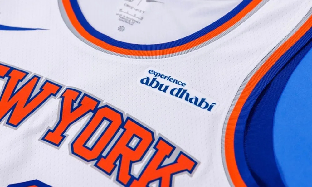 Close-up of a New York Knicks basketball jersey displaying the “Experience Abu Dhabi” sponsor patch above the team name.
