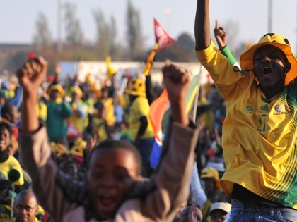 Euphoric fans in Bafana Bafana colors celebrate and cheer with colorful paraphrenalia. 