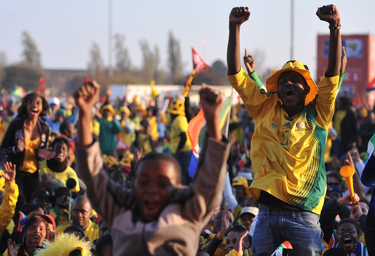Euphoric fans in Bafana Bafana colors celebrate and cheer with colorful paraphrenalia. 