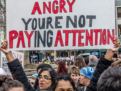 Protester holding an 'If you're not angry, you're not paying attention' sign at a Women's March rally.