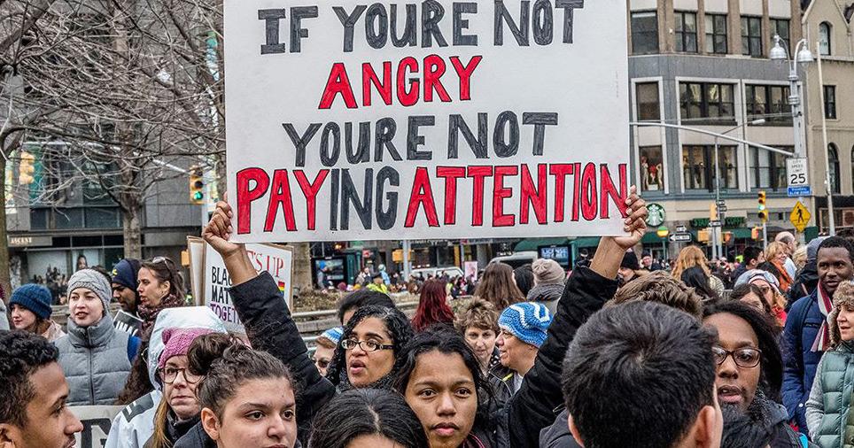 Protester holding an 'If you're not angry, you're not paying attention' sign at a Women's March rally.