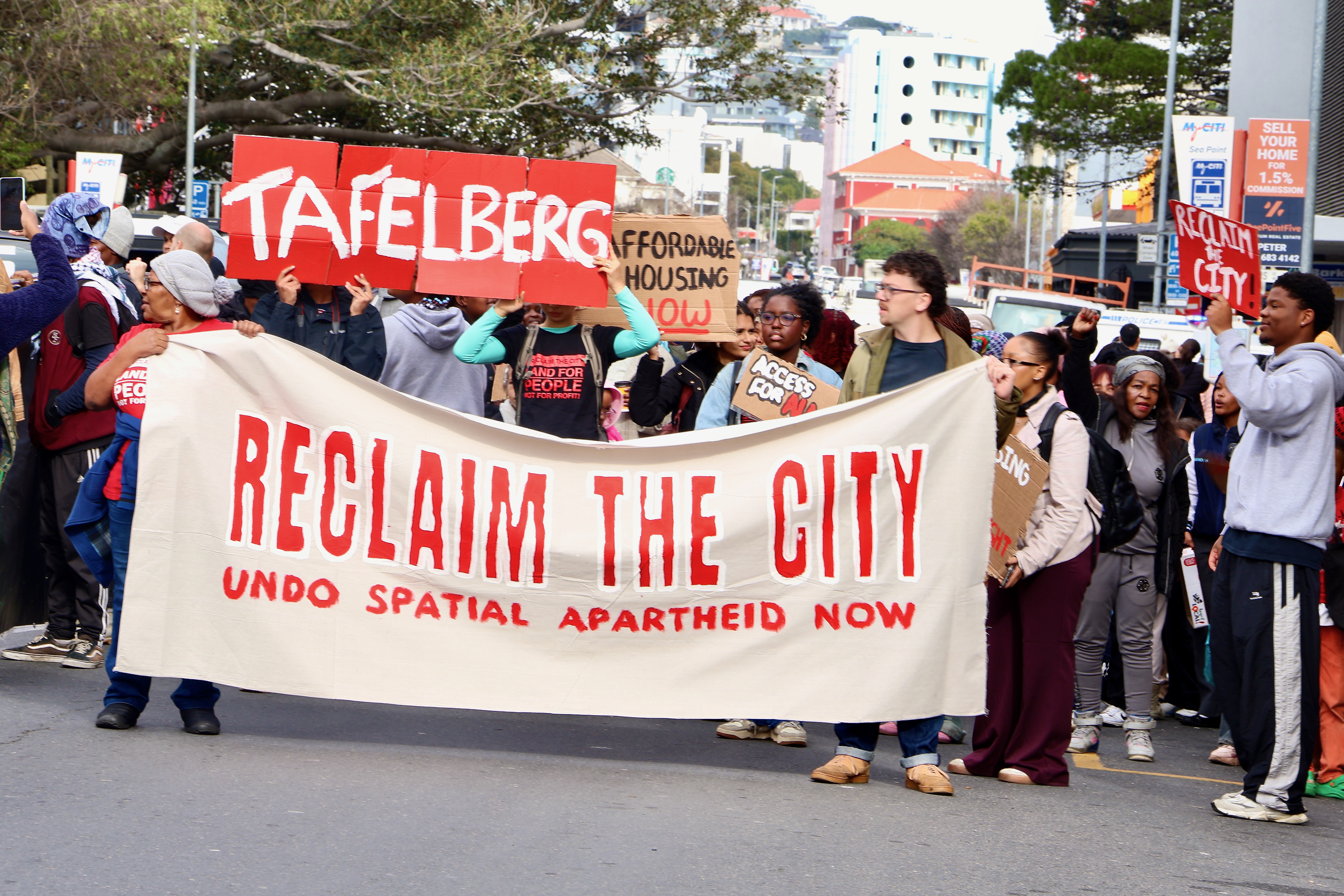 Housing activists march through Sea Point carrying a large banner reading “Reclaim the City: Undo Spatial Apartheid Now” alongside placards calling for affordable housing and the redevelopment of the Tafelberg site.