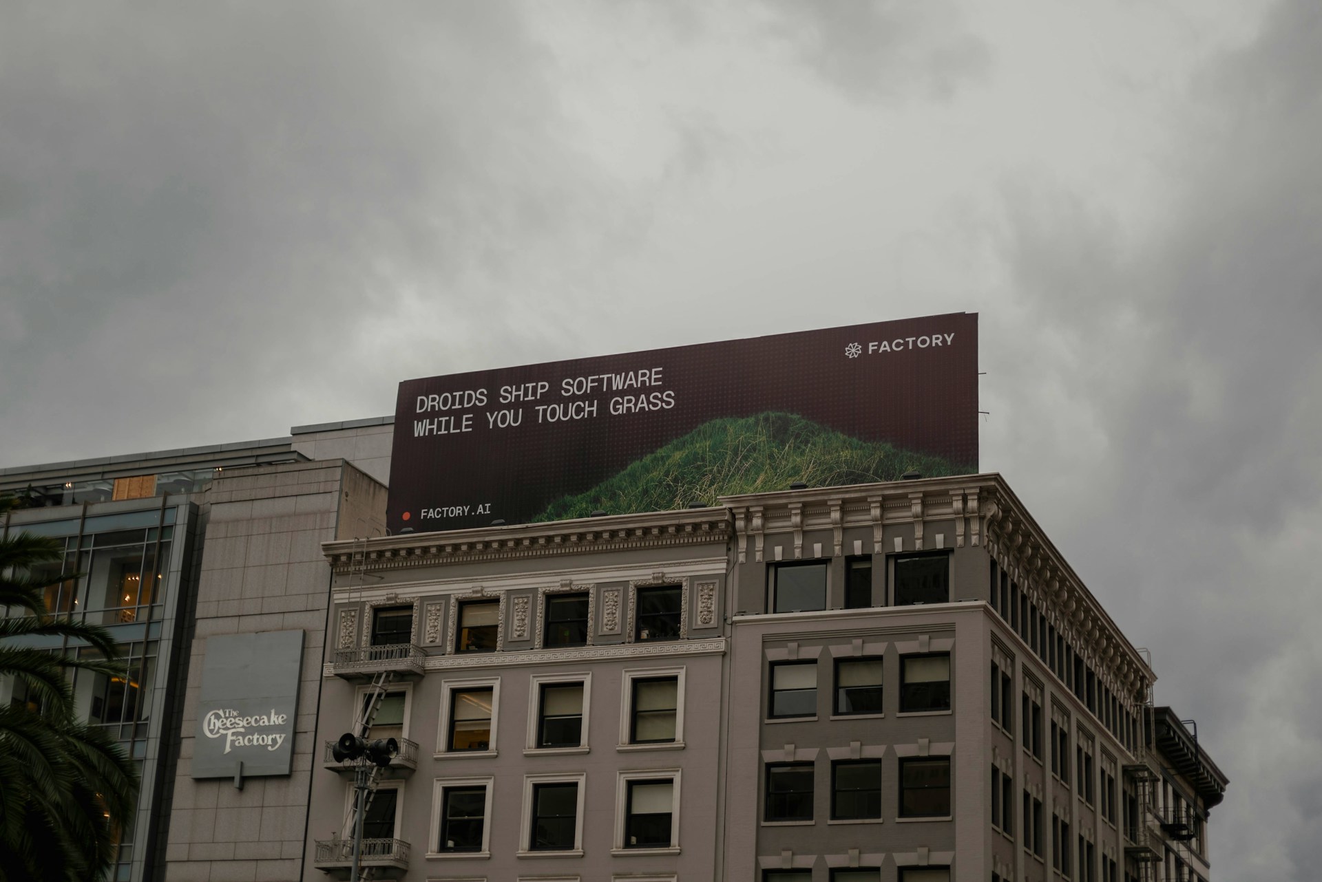 A billboard on a building in San Francisco, California, depicts an advertisement reading, "Droids ship software while you touch grass"
