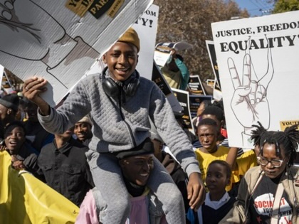 A smiling young protester sits on another participant’s shoulders while demonstrators march with placards calling for justice, freedom, and equality during a Youth Day protest in Pretoria.