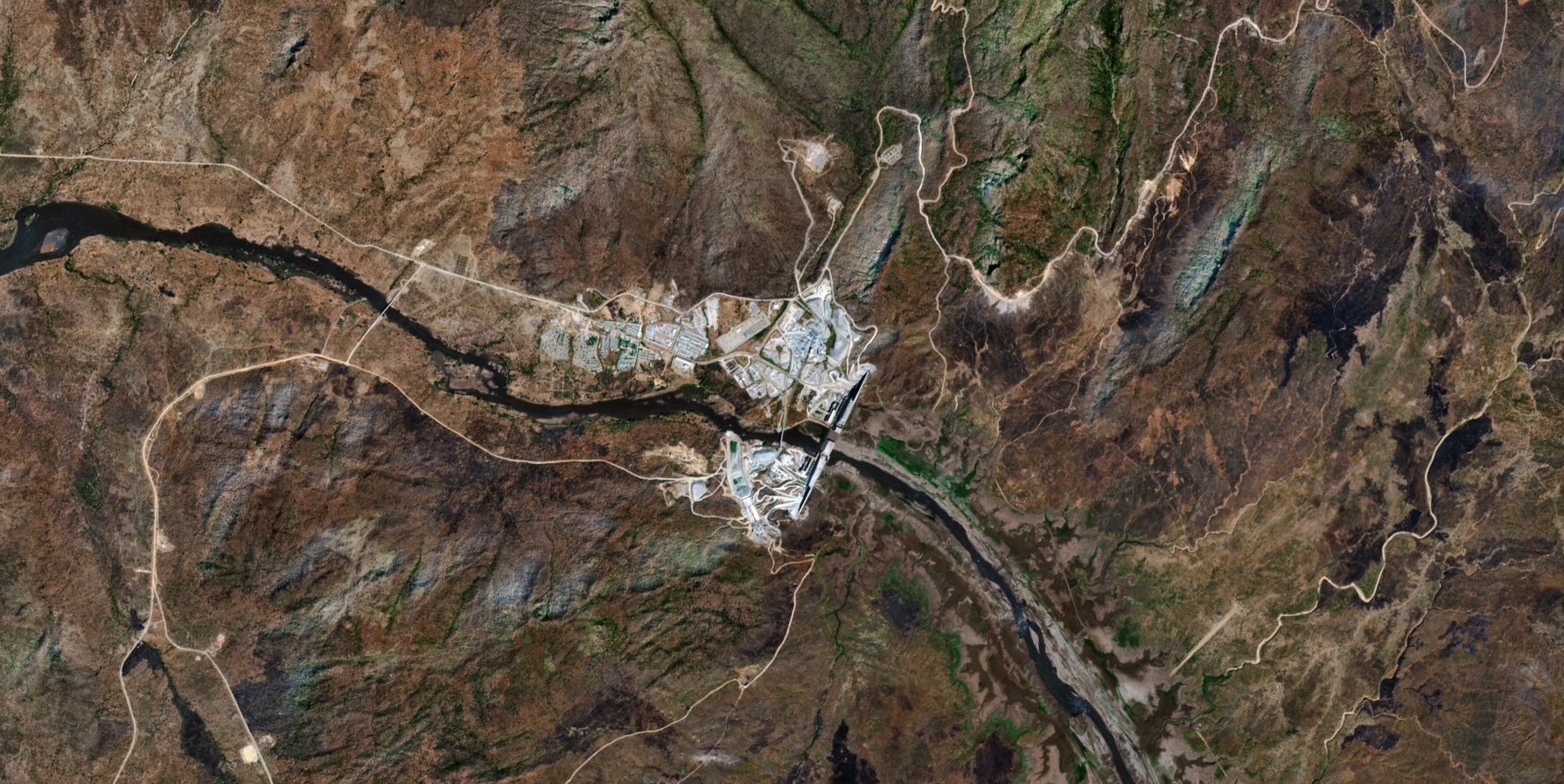 Satellite image of the Grand Ethiopian Renaissance Dam spanning the Blue Nile in a mountainous, arid landscape, with access roads and construction areas visible around the site.