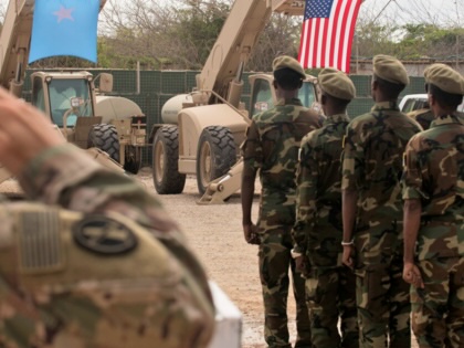 A U.S. soldier salutes as a formation of Somali soldiers stand at attention facing the Somali and U.S. flags, which hang from military vehicles during a joint ceremony in Somalia.