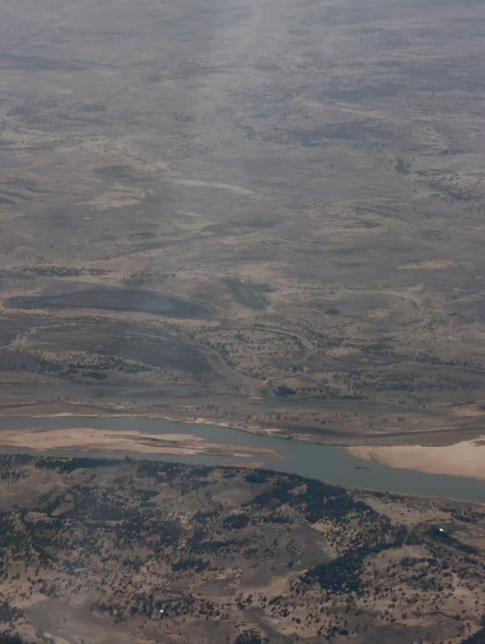 An aerial view of the Chadian landscape, with the Chari River winding through a dry, sparsely vegetated plain as seen from an airplane.