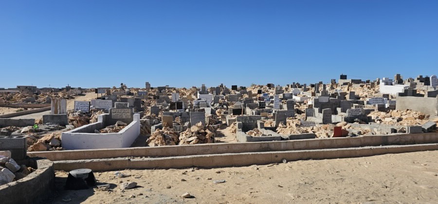 A collection of unmarked, dilapidated graves under a bright, blue, sunny sky