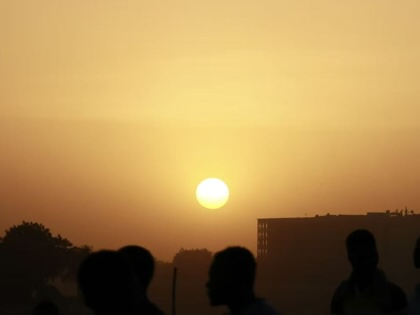 Silhouettes of pedestrians walking at sunset in N'Djamena, with the low sun glowing above the city skyline.