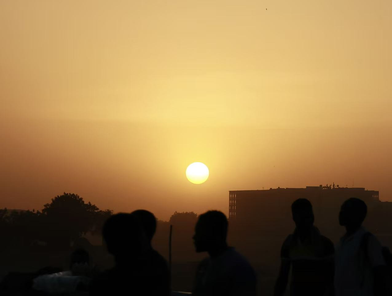 Silhouettes of pedestrians walking at sunset in N'Djamena, with the low sun glowing above the city skyline.